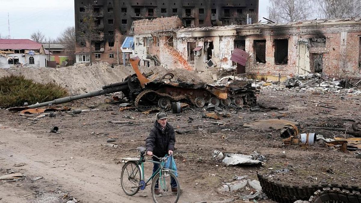 Ein Anwohner fährt mit seinem Fahrrad vor beschädigten Gebäuden und einem Panzer in der Stadt Trostianets vorbei, 28. März 2022 .