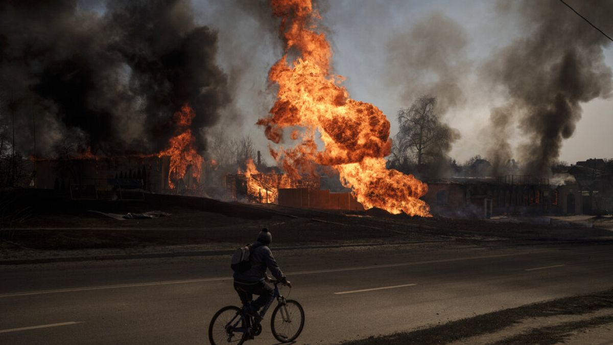 Un hombre pasa con su bicicleta entre las llamas y el humo que se eleva de un incendio tras un ataque ruso en Jarkov, Ucrania