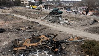 Des habitants passent devant des chars russes endommagés et un monument pour la Seconde Guerre Mondiale dans la ville de Trostyanets à l'est de Kyiv, le 28 mars 2022