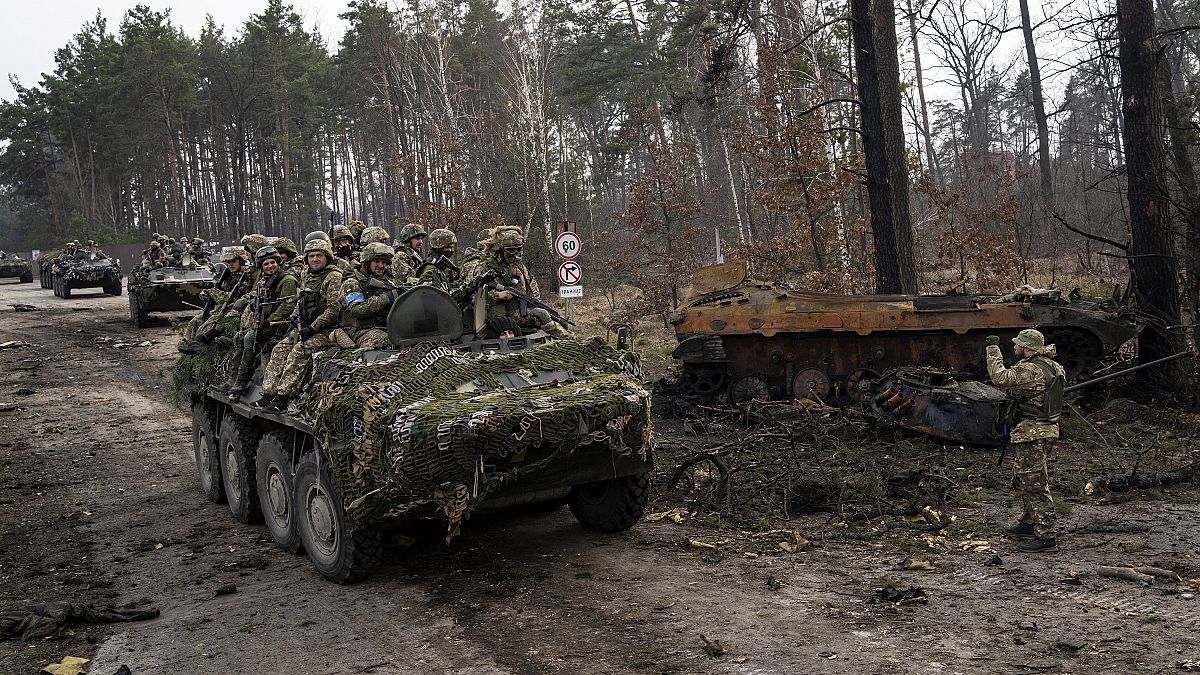 Ουκρανοί στρατιώτες σε τεθωρακισμένο μεταφοράς προσωπικού περνούν δίπλα από κατεστραμμένο ρωσικό άρμα στα περίχωρα του Κιέβου