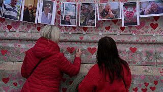 Family members write a message to two sisters who died of COVID on the National Covid Memorial wall in London, Tuesday, March 29, 2022.