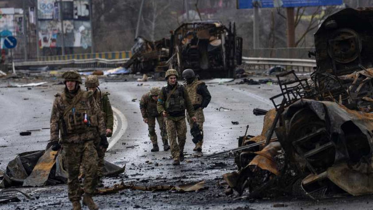 Ukrán katonák megsemmisült orosz páncélozott katonai járművek roncsai mellett Bucsában