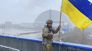 Egy katona az ukrán lobogóval a csernobili erőmű szarkofágja előtt