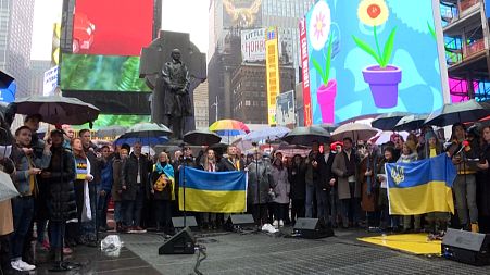 Members of the Broadway theatre community singing 'Do You Hear The People Sing?' in Times Square, holding Ukrainian flags in the rain