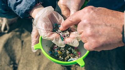 People investigating small pieces of plastic found on a beach.