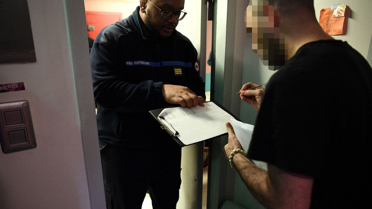An inmate (R) signs a register of electors after receiving presidential candidates manifestos in his cell from prison guards at the Fleury-Merogis prison