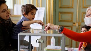 Uma mulher segura uma criança que deposita o voto numa urna das Presidenciais francesas