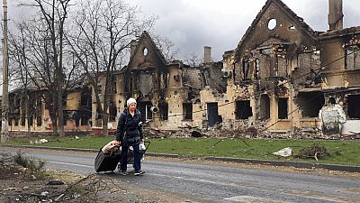 Женщина идёт мимо домов, поврежденных во время боевых действий в восточном Мариуполе, Украина, пятница, 8 апреля 2022 г