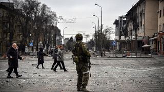 People pass by a Russian soldier in central Mariupol on April 12, 2022, as Russian troops intensify a campaign to take the strategic port city