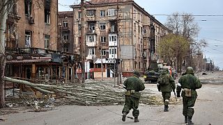 Servicemen of Donetsk People's Republic militia walk past damaged apartment buildings in an area controlled by Russian-backed separatist forces in Mariupol, April 16, 2022.