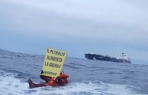 Protesters on rubber dinghy holding placard reading "Oil fuels war"