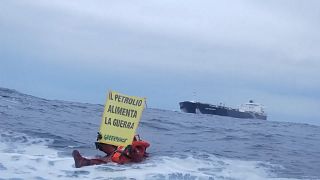 Protesters on rubber dinghy holding placard reading "Oil fuels war"