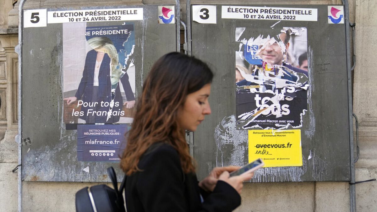 Junge Frau in Paris vor abgerissenen Wahlplakaten von Macron und Le Pen