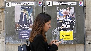 Junge Frau in Paris vor abgerissenen Wahlplakaten von Macron und Le Pen
