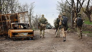 Servicemen of Donetsk People's Republic militia walk past damaged vehicles in an area controlled by Russian-backed separatist forces in Mariupol, April 19, 2022.