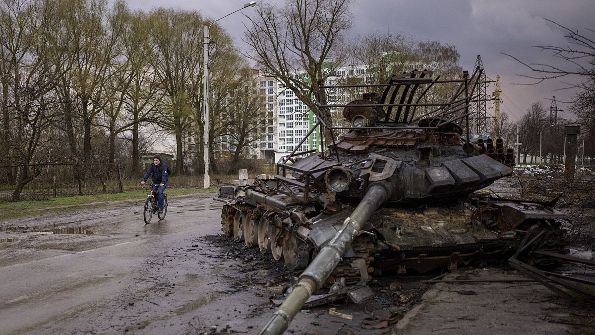 Egy férfi biciklizik el egy tönkretett tank mellett Csernyihiv városában