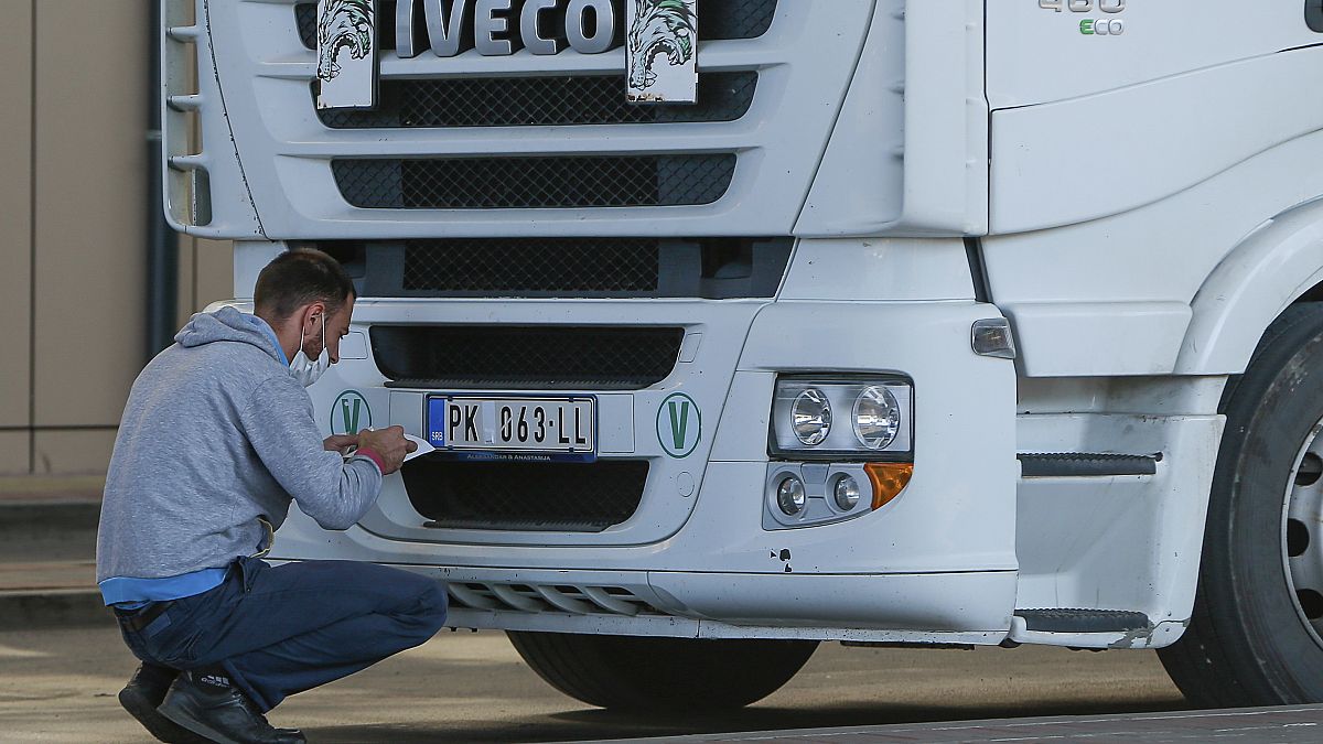 A truck driver places stickers on number plates at the Merdare border crossing on Monday, Oct. 4, 2021.