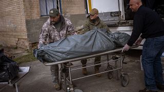 متطوعان أمريكيان ويد هيلتون وداريل لوفليس  يساعدان في نقل جثمان نحو المشرحة المركزية في بوتشا، بضواحي كييف، الإثنين، 25 أبريل 2022