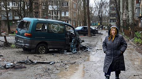 A Mariupol resident walks past a damaged vehicle marked with the letter Z.