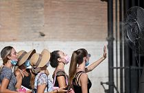 A group of woman cool off in front of a cooling fan during a heatwave as they queue at the enterance of the Colosseum in Rome.