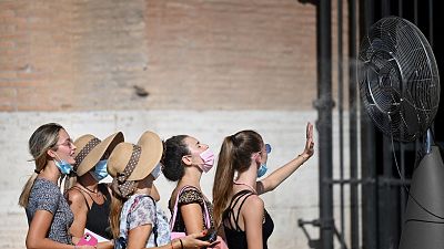 A group of woman cool off in front of a cooling fan during a heatwave as they queue at the enterance of the Colosseum in Rome.