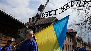 Ukrán zászlót tartó nő az auschwitzi koncentrációs tábor kapujánál 2022. április 28-án