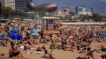 People sunbathe on a beach in Barcelona, Spain. 