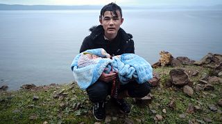 In this Thursday, March 5, 2020, file photo, a migrant holding a baby pauses on the side of the road while walking to the village of Skala Sikaminias, in Lesbos.