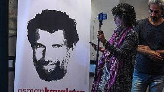 A journalist stands in front of a poster featuring jailed businessman and philanthropist Osman Kavala.