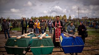 Un prêtre bénit les dépouilles de trois personnes tuées par les forces russes, Boutcha, Ukraine, 27 avril