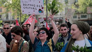 Demonstrators hold bouquet with sign reading  "Work tires even the donkeys, Let's stay beavers" during a May Day demonstration march.