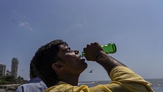 Un homme boit un soda au cours d'une promenade sur les côtes de la mer d'Arabie à Mumbai, Inde (1er mai 2022).