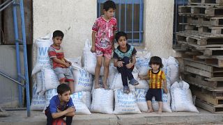 Children sit on bags of rice from the World Food Program (WFP) at a school that serves as a shelter for internally displaced people in Baghdad's eastern district of Jamila.