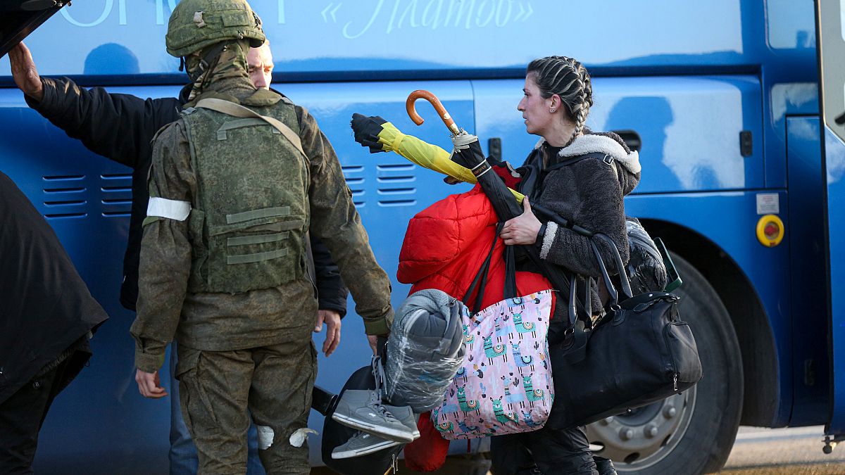  امرأة تنغادر مأوى في آزوفستال تسير نحو حافلة برفقة جندي من ميليشيا جمهورية دونيتسك الشعبية في ماريوبول. 2022/05/06
