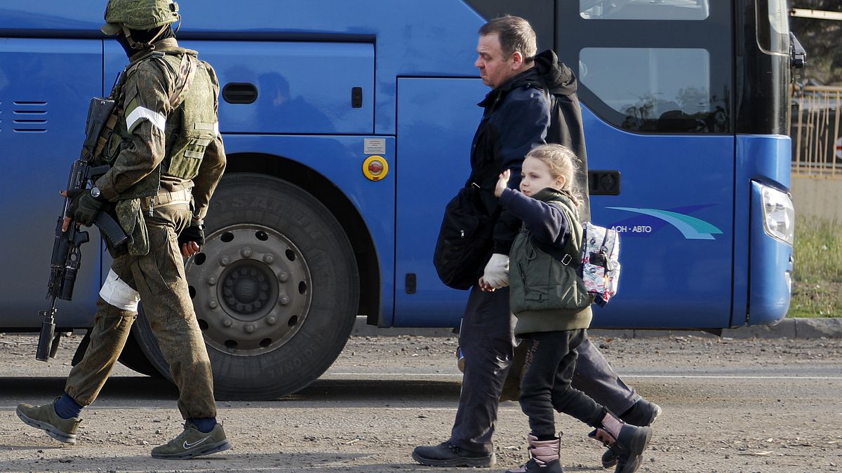 Ein Mann und ein Kind werden von einem russischen Soldaten zumBus begleitet.