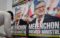 A supporter of far-left leader Jean-Luc Melenchon sticks electoral posters reading "Melenchon Prime Minister" before a local meeting, Thursday, May 5, 2022 in Lille.