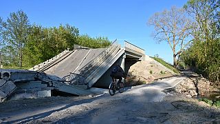 Un ucraniano pasa en bicicleta junto a un puente destruido