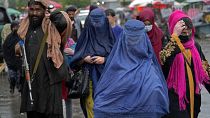 Des femmes afghanes traversant le vieux marché de Kaboul alors qu'un combattant taliban monte la garde, le mardi 3 mai 2022.