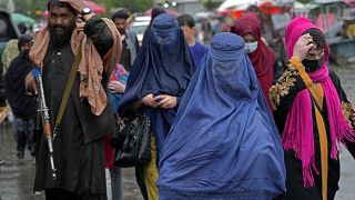 Des femmes afghanes traversant le vieux marché de Kaboul alors qu'un combattant taliban monte la garde, le mardi 3 mai 2022.