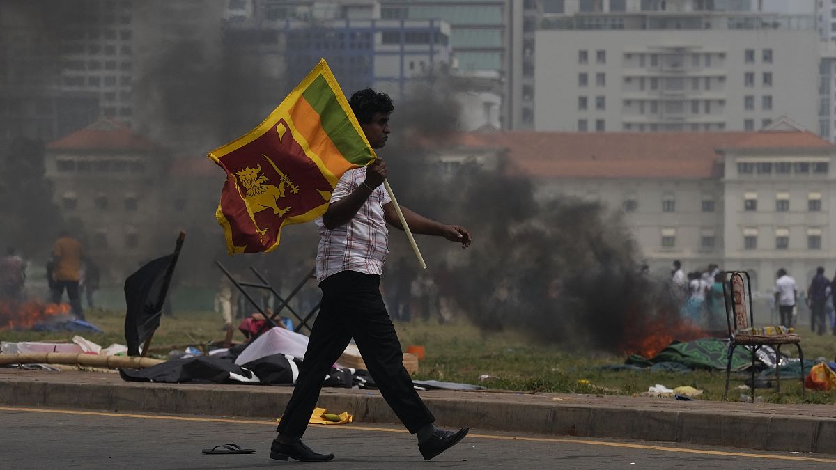Сторонник правительства Шри-Ланки несёт национальный флаг. Видны следы поджога палаточного лагеря оппозиционеров возле резиденции президента в Коломбо.