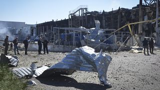 People stand near a destroyed building on the outskirts of Odesa, Ukraine, Tuesday, May 10, 2022. A shopping centre and a warehouse were destroyed in the Russian strike.