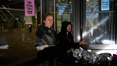 An Extinction Rebellion climate change protester sits with a lock around her neck attached to a bar on a door. An Extinction Rebellion climate change protester sits with a lock around her neck attached to a bar on a door.