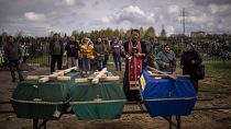 A priest blesses the remains of three people who died during the Russian occupation and were disinterred from temporary burial sites in Bucha, on the outskirts of Kyiv.
