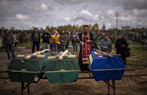 A priest blesses the remains of three people who died during the Russian occupation and were disinterred from temporary burial sites in Bucha, on the outskirts of Kyiv.