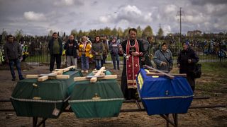 A priest blesses the remains of three people who died during the Russian occupation and were disinterred from temporary burial sites in Bucha, on the outskirts of Kyiv.