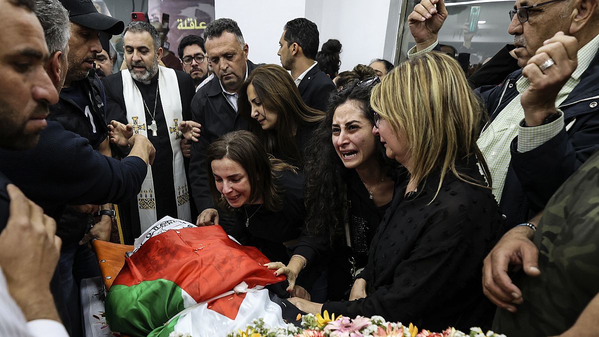 Colleagues and friends react as the Palestinian flag-draped body of veteran Al-Jazeera journalist Shireen Abu Akleh is brought to the news channel's office in Ramallah