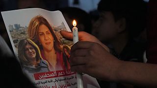 فلسطيني يحمل شمعة وصورة شيرين أبو عاقلة صحفية الجزيرة التي تم اغتيالها، أمام مكتب الجزيرة في مدينة غزة.