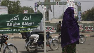 سيدة مسلمة تمر بجانب لافتة كتب عليها "الله أكبر" في كاتسينا، نيجيريا.