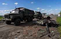 Ukrainian army vehicles drive past the remains of a Russian tank in north Kharkiv, east Ukraine, Friday, May 13, 2022.