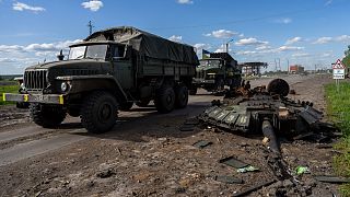 Ukrainian army vehicles drive past the remains of a Russian tank in north Kharkiv, east Ukraine, Friday, May 13, 2022.